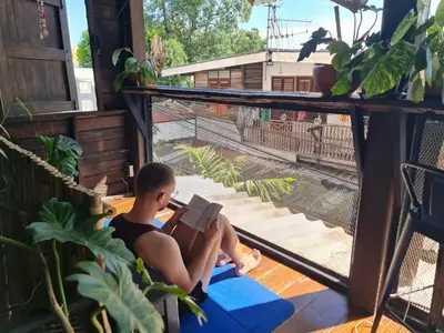a man sitting on a balcony reading a book at Non House Bangkok บ้านนอนโฮสเทล in Bangkok