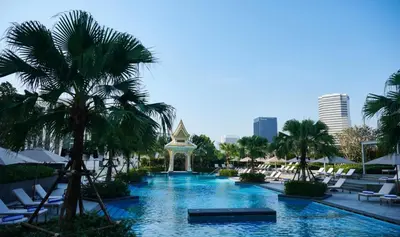 a swimming pool with chairs and palm trees in a resort at Chatrium Grand Bangkok in Bangkok