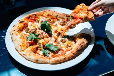a person eating a slice of pizza on a plate at Public House Bangkok, a Member of Design Hotels in Bangkok